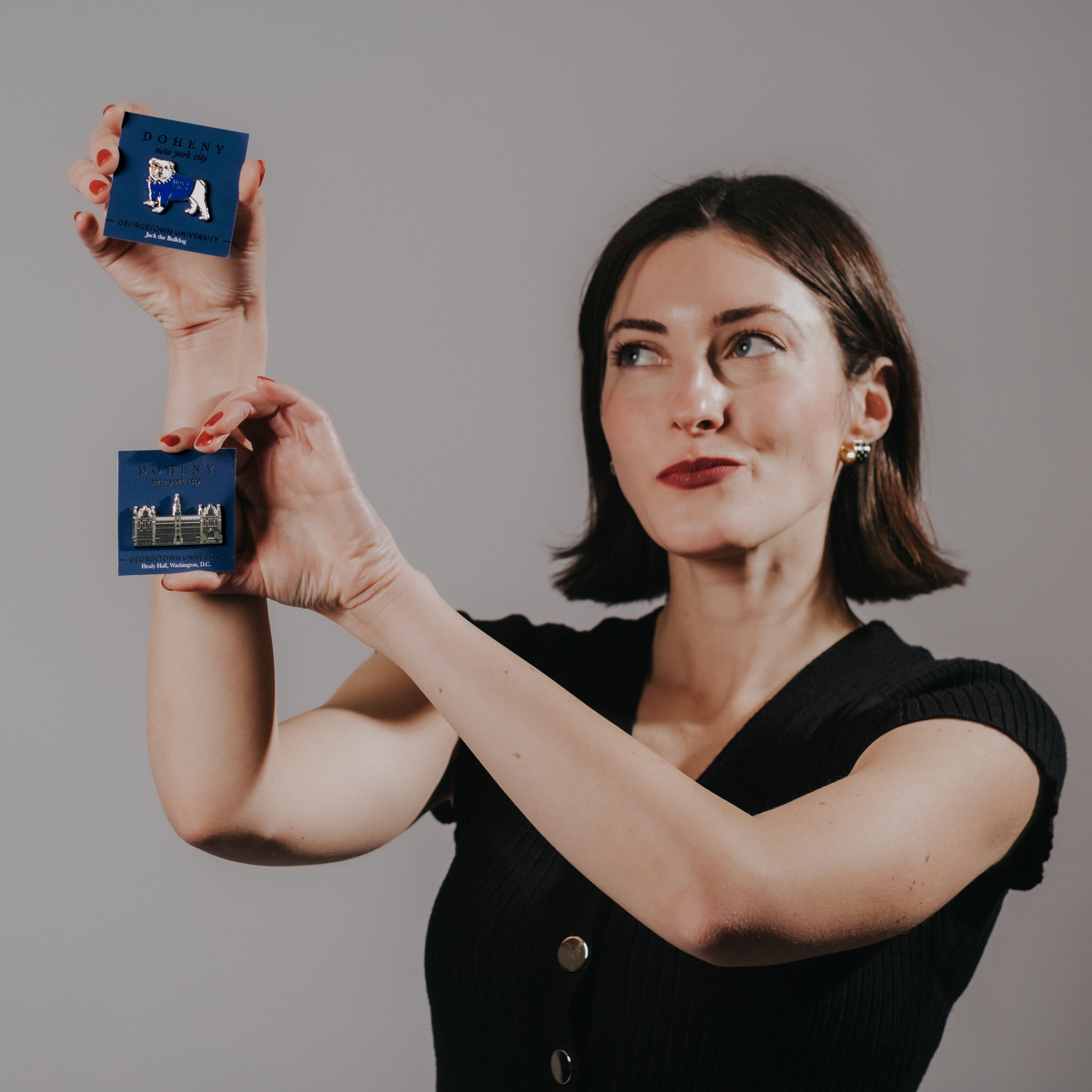 Owner of Doheny NYC holding two lapel pins that represent Jack the Bulldog and Healy Hall of Georgetown University